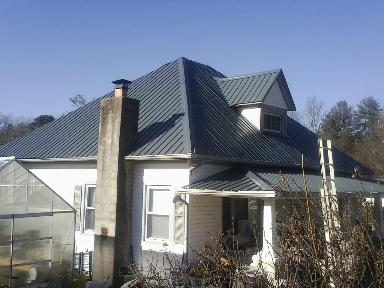 Dark blue standing seam metal roof on a white farmhouse with dormer — Slate & Tile Roof Repair by Roofing Brothers in Ward