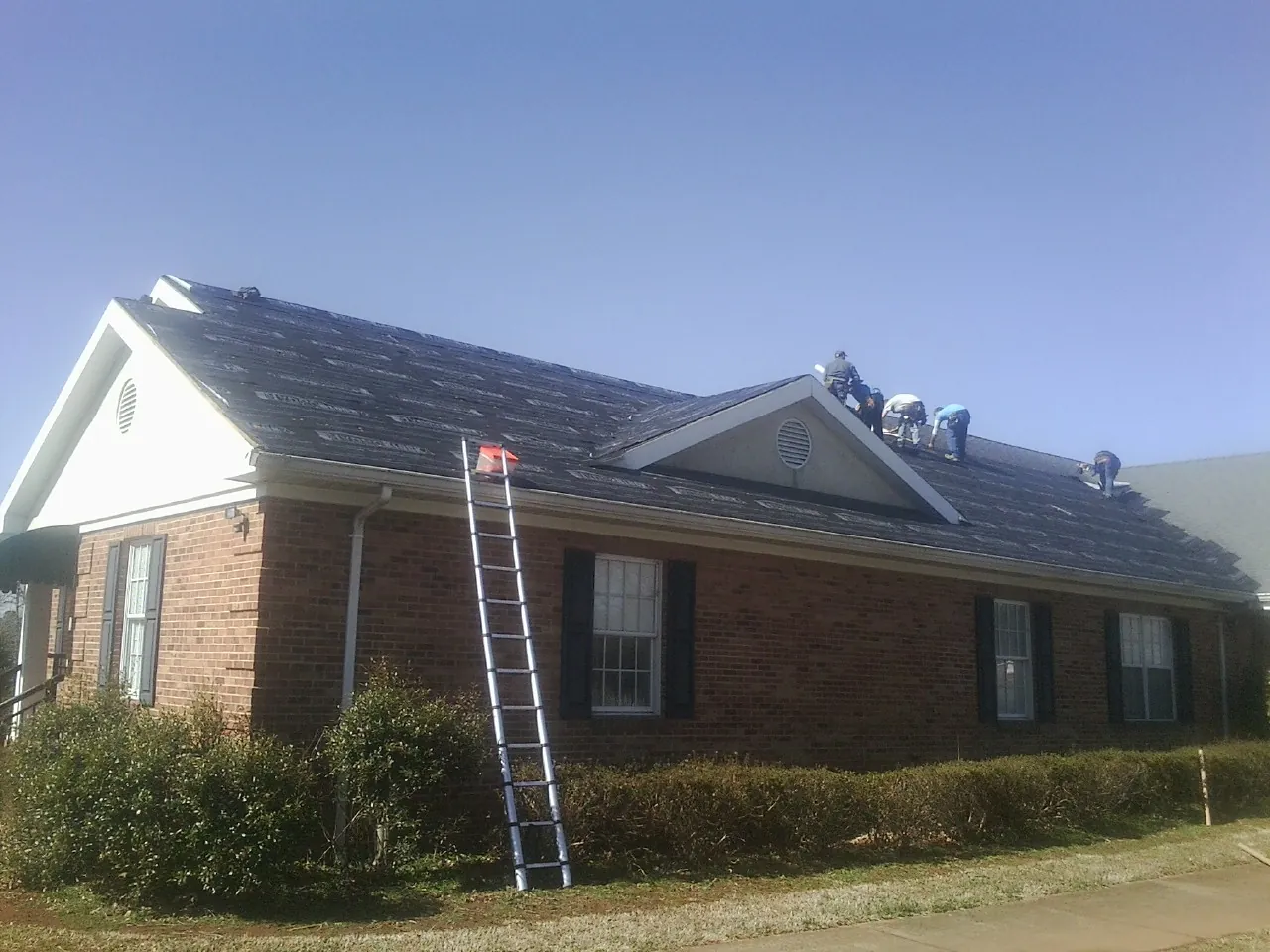 Crew tearing shingles off a brick ranch roof with a ladder set — Emergency Roof Repair work by our crew in Ward