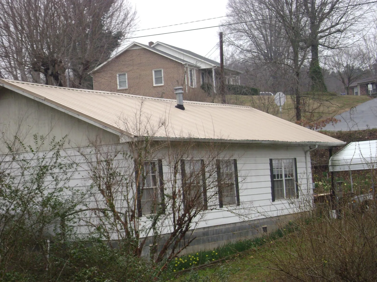 Tan metal roof on a white sided house set into a hillside — Commercial Roofing by Roofing Brothers in Ward